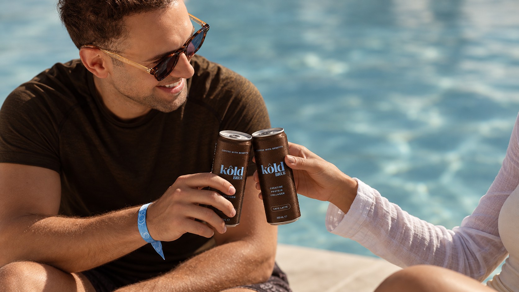 Two friends toasting KôldBrue cans poolside