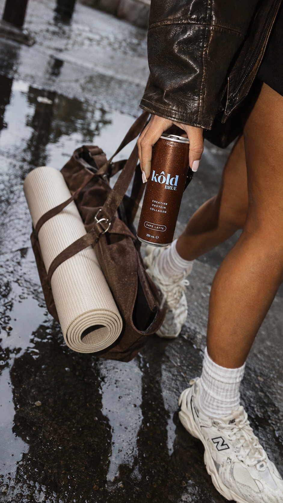 Someone holding a KôldBrue can next to a rolled yoga mat and gym bag